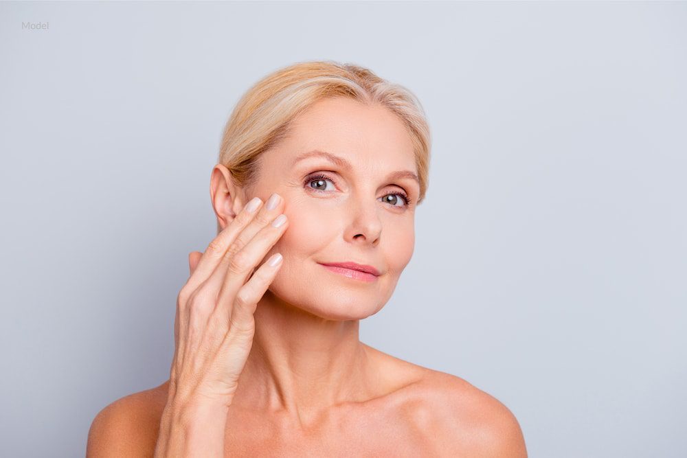 Middle aged woman touching and examining her face for signs of aging.