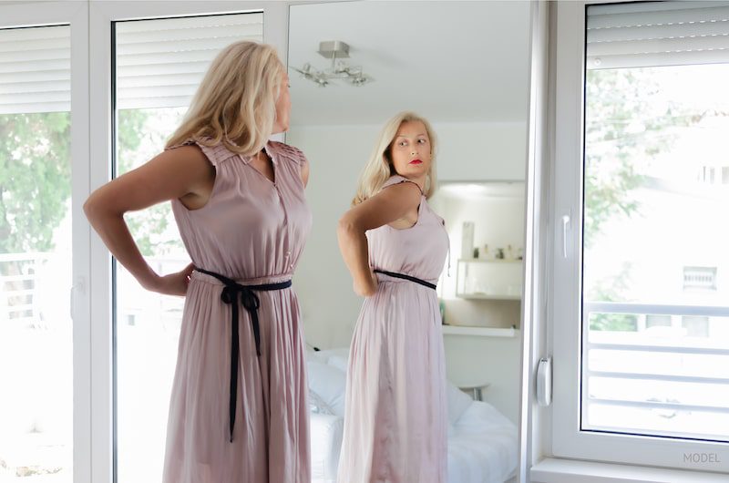 Woman looking at herself in the mirror while considering plastic surgery.