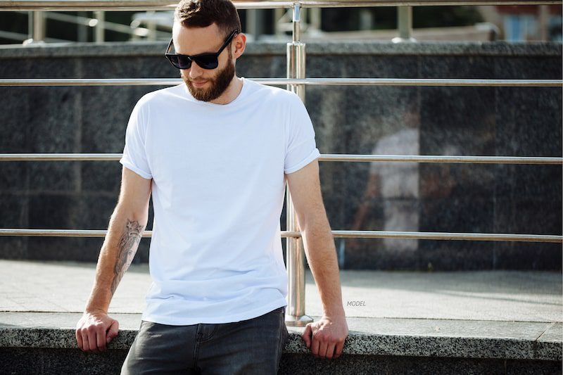 Man sitting on half-wall, wearing a white t-shirt