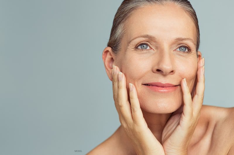 Beautiful mature woman smiling as she places both hands on the sides of her face.