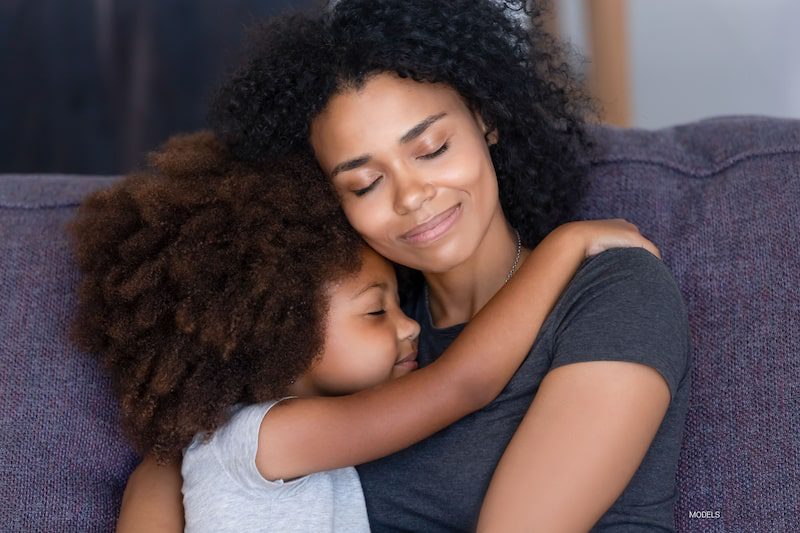 Mother hugging her daughter while sitting on sofa.