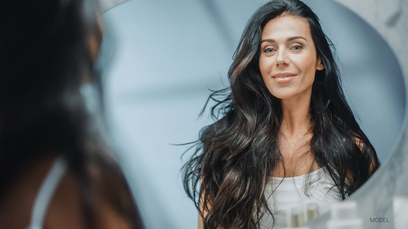 Beautiful middle-aged woman with dark hair looking in the mirror and smiling