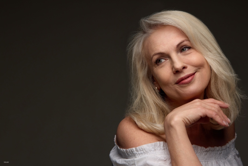 Senior woman smiling gently and resting chin on hand against dark background